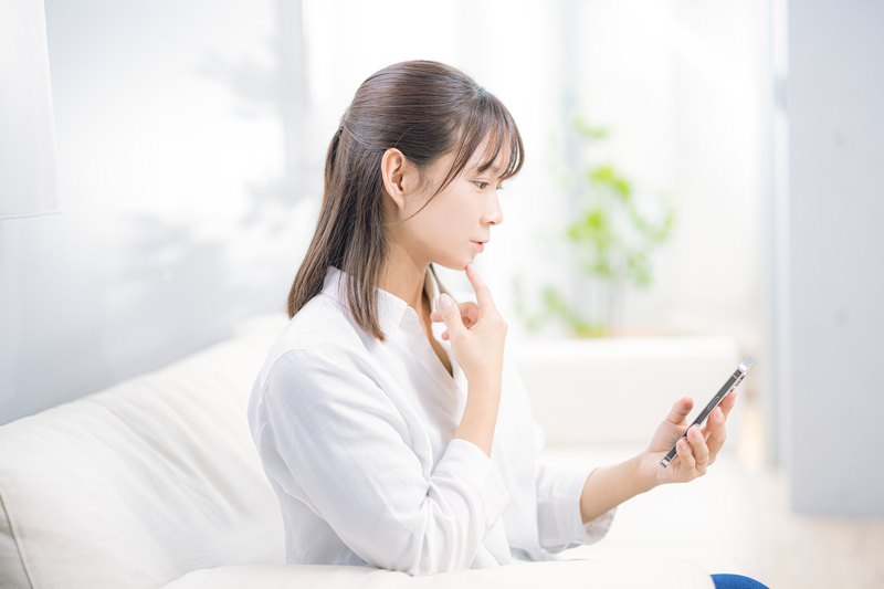 スマホを見ながら考える女性（売上チェックのイメージ）